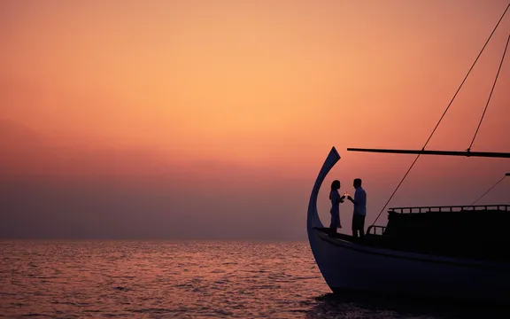 Couple enjoying wine together on a boat deck with a scenic view at One&Only Reethi Rah